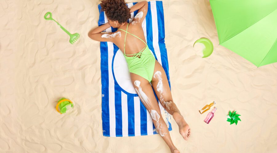 Foto tirada de mulher na praia deitada com protetor nas pernas